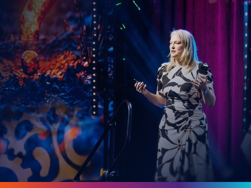 "Speaker presenting on stage in a floral dress at a legal ops conference, with colorful stage lighting in the background"